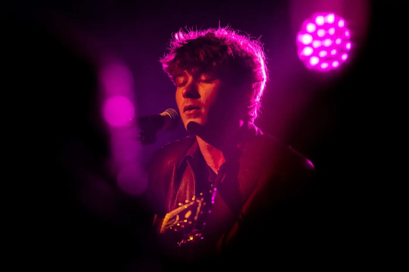Cameron singing under a magenta light