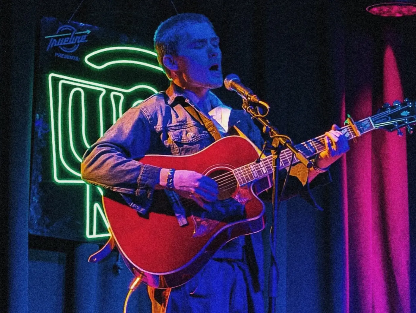 Cameron singing in front of a green neon sign